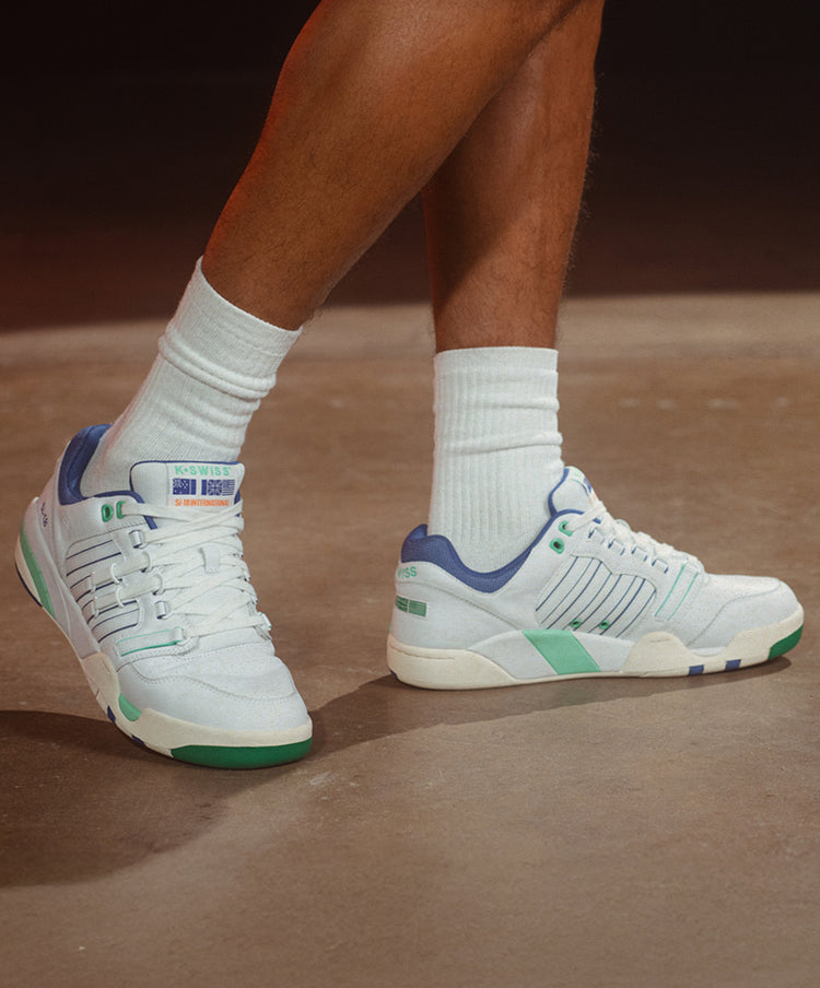 Close-up of man's feet in K-Swiss sneakers with green and blue accents and white athletic socks