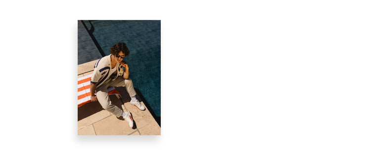 Image of a young man sitting on a lounge chair near a pool wearing preppy clothing and K-Swiss sneakers