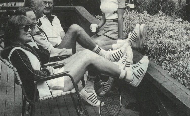 Black and white image of four people at a tennis club with their feet on a ledge wearing K-Swiss shoes