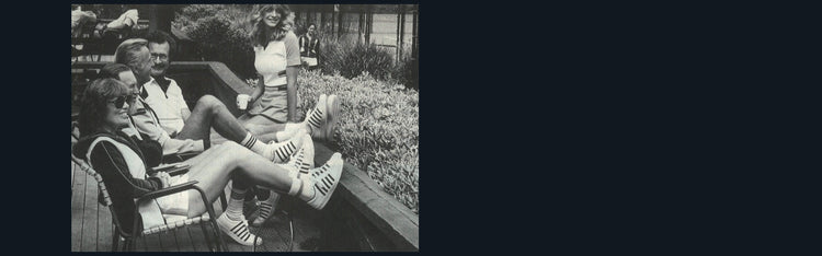 Black and white image of four people at a tennis club with their feet on a ledge wearing K-Swiss shoes