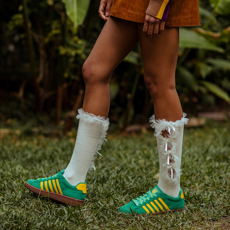 Person wearing green and yellow K-Swiss Court Tiebreak II sneakers with white socks on grass