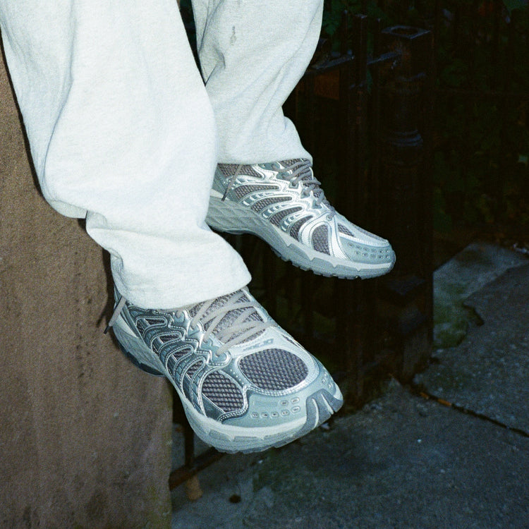 Person wearing gray athletic shoes - the KSRC Konejo - with white pants sitting on a bench.