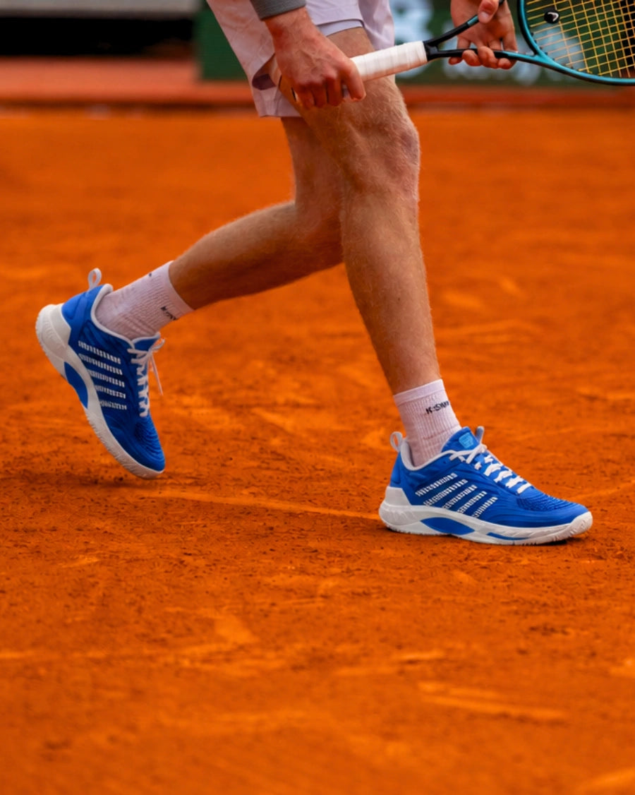 Person wearing blue and white athletic shoes on a clay tennis court