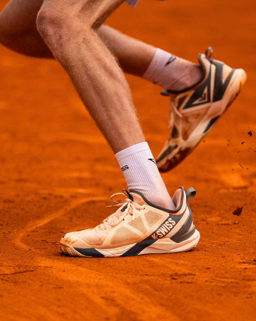 Close-up of tennis shoes on a clay court with Swiss brand logo.
