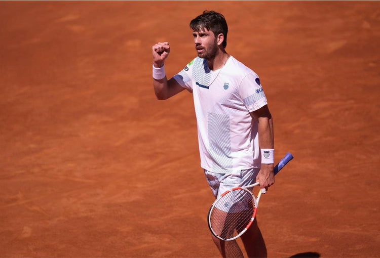 Cameron Norrie holding up a fist in celebration on a clay tennis court while wearing K-Swiss clothing