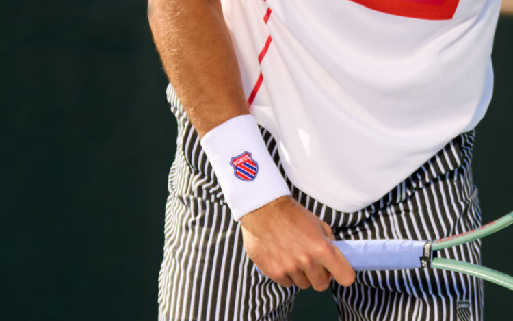 Close up on a man's wrist and hand holding a tennis racket and wearing a K-Swiss wrist band