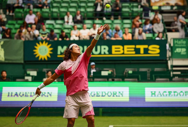 Zhizhen Zhang serving in a tennis match while wearing K-Swiss clothing