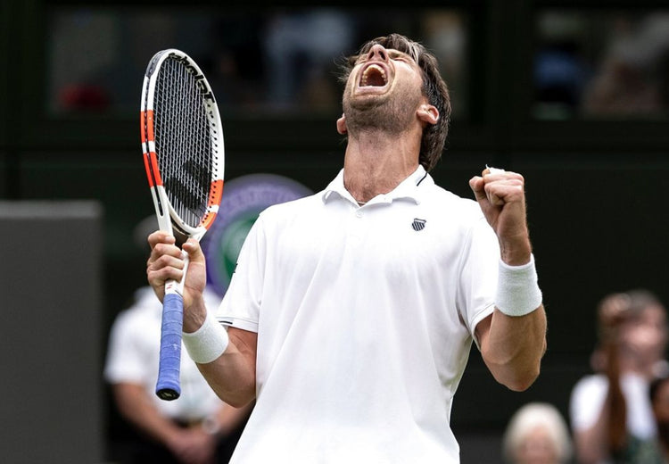 Cameron Norrie celebrating while holding a tennis racket and wearing a K-Swiss polo shirt