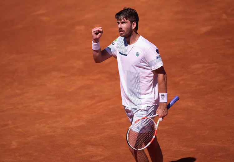 Cameron Norrie holding up a fist in celebration on a clay tennis court while wearing K-Swiss clothing