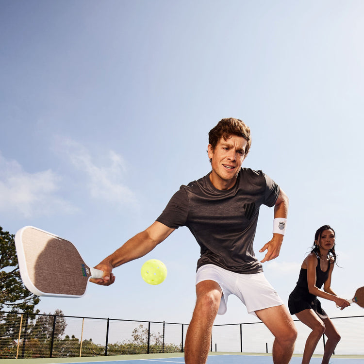 Image of a man in K-Swiss clothing playing pickleball with a woman in the background playing next to him