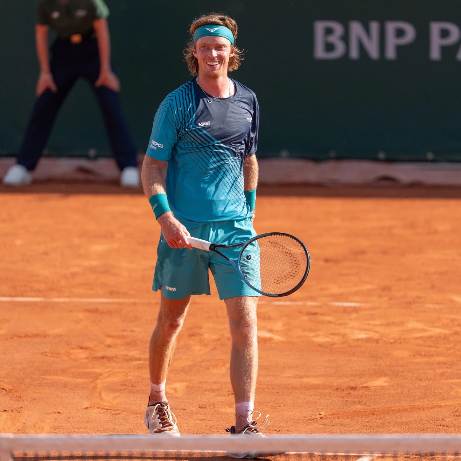 Tennis player in blue outfit holding a racket on a clay court with BNP Paribas branding.