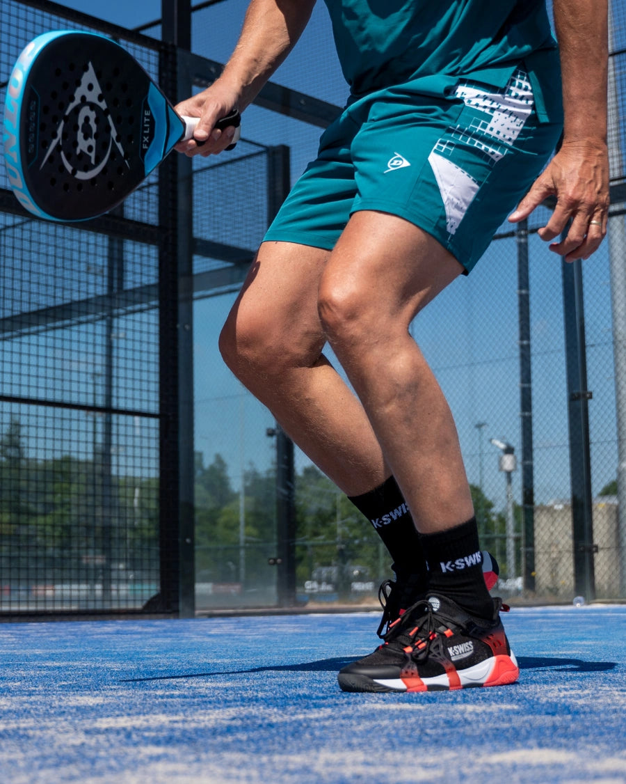Person playing padel on a blue court with a racket and sports attire.